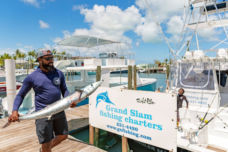 Fishing captain holding a large wahoo on a marina dock. 