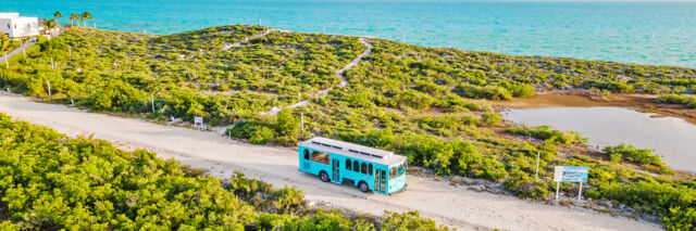 A turquoise trolley driving near the ocean in Turks and Caicos. 