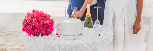Couple cutting a wedding cake on the beach.