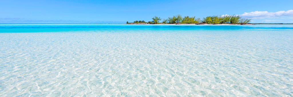 Clear waters of Horsestable Beach on North Caicos, with a small island in the distance.