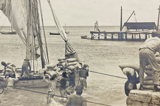 Loading bagged sea salt onto a small sailboat, circa 1926