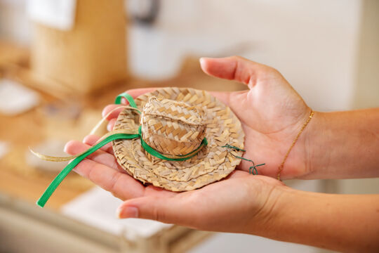 Hands holding a miniature straw hat.