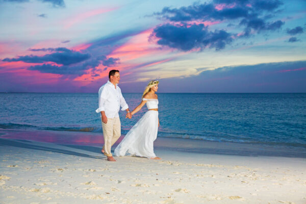 Newlywed couple walking down a beach at sunset.