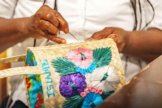 Woman stitching a straw handbag.