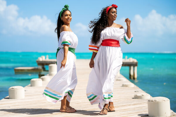 Two women wearing white dresses with colorful ribbons on a wooden dock. 
