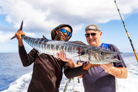A captain and guest holding a large wahoo onboard. 