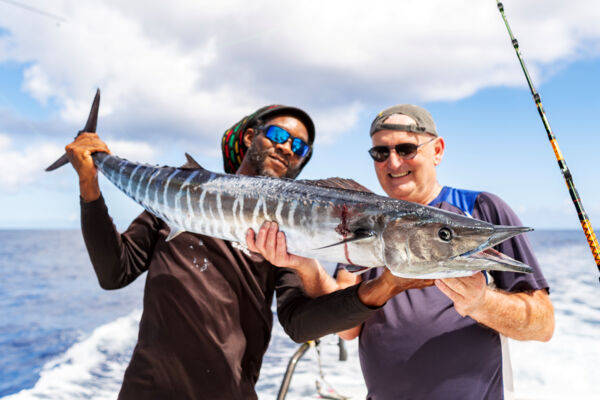 A captain and guest holding a large wahoo onboard. 