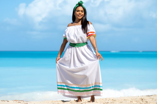 Woman wearing a white dress and green sash on a beach dune. 