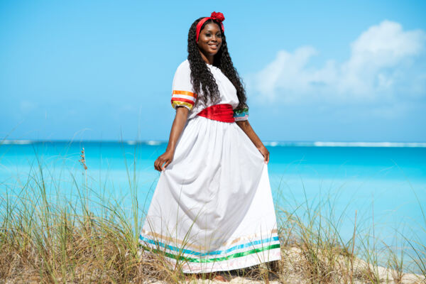 Woman wearing a white dress and red sash on a beach.