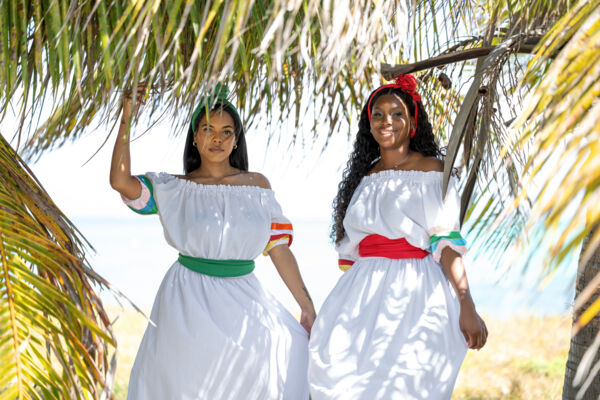 Women under palm trees wearing the national costume of the Turks and Caicos Islands.