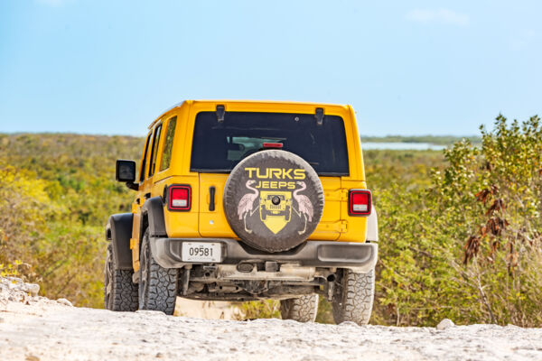 A yellow Jeep Wrangler driving down a hill.