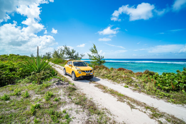 Yellow car driving along a sandy path near the ocean.