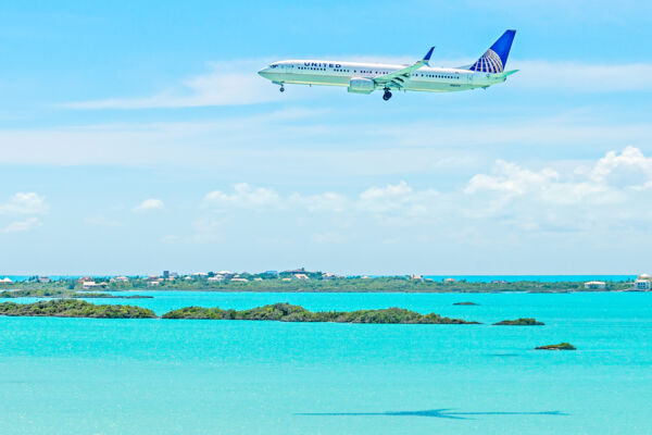 United Airlines jet flying over a turquoise lagoon in Turks and Caicos.
