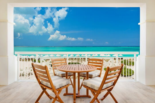 Dining table on a balcony overlooking turquoise water and a white-sand beach