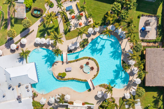 Overhead view of a turquoise pool surrounded by loungers and palm trees