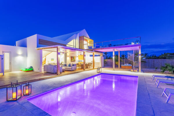 Modern villa and pool with pink lighting at night.