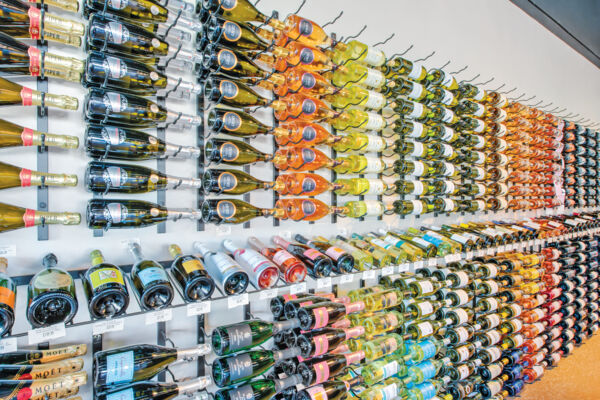 Sparkling wine, red wine, and white wine bottles displayed on a wall rack inside a store. 