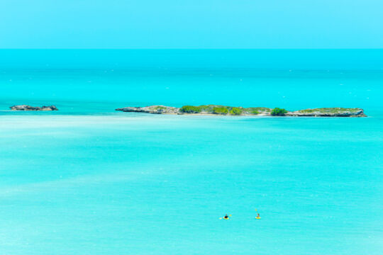 Kayakers approaching a few rocky islands in turquoise blue water