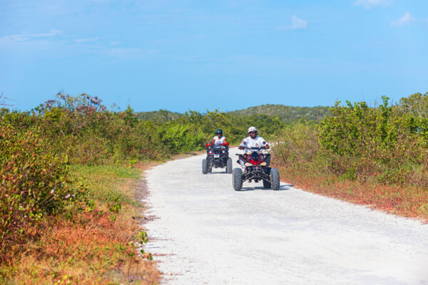 Two people riding ATVs down a dirt road in Turks and Caicos. 