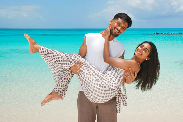 Man lifting up a woman on a beach with turquoise water