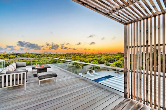 A wooden balcony with a fireplace overlooking tropical vegetation and a beautiful sunset.