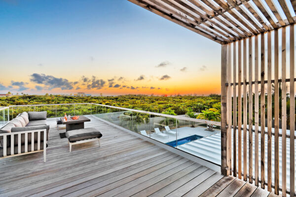 A wooden balcony with a fireplace overlooking tropical vegetation and a beautiful sunset. 