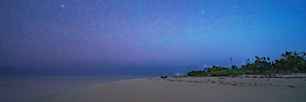 Beach at night with stars and constellations.
