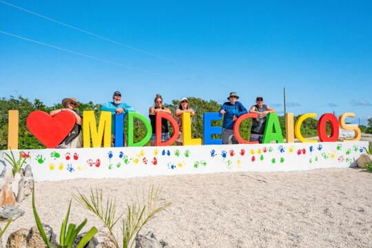 People posing with a sign that says 'I love Middle Caicos'.