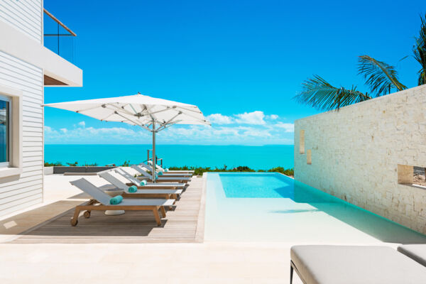 Modern pool deck and infinity pool overlooking turquoise ocean at a luxury villa. 